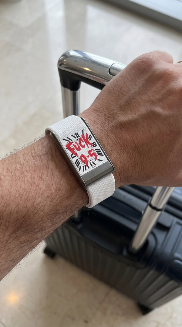 QUIETUDE Fuck 9-5 band in white worn on the wrist, hand on a cabin suitcase handle