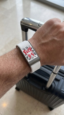 Bracelet QUIETUDE blanc porté au poignet, main sur une valise cabine